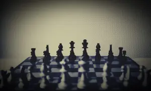 Szachownica z czarnymi figurami w pierwszym rzędzie, w tle białe figury.
