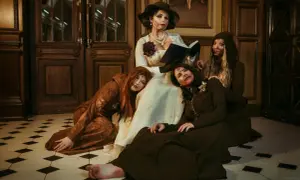 Daughters of Lady Dimitrescu, w makijażu sugerującym rany, siedzą i leżą wokół matki czytającej książkę.