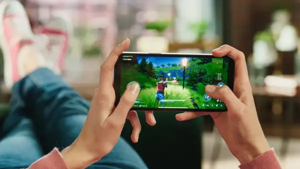 Dłonie trzymające smartfon z grą akcji w zielonym, bajkowym świecie.