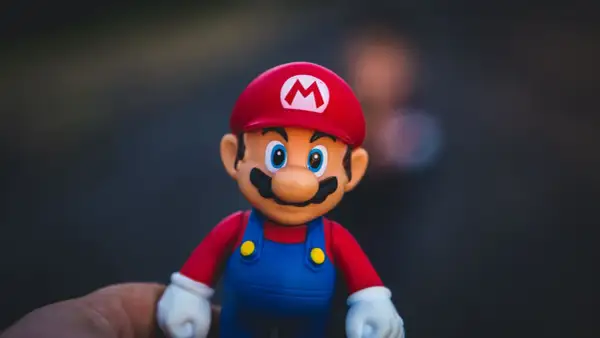 Figurka Mario w czerwonej czapce z literą M i niebieskich ogrodniczkach, trzymana na dłoni.